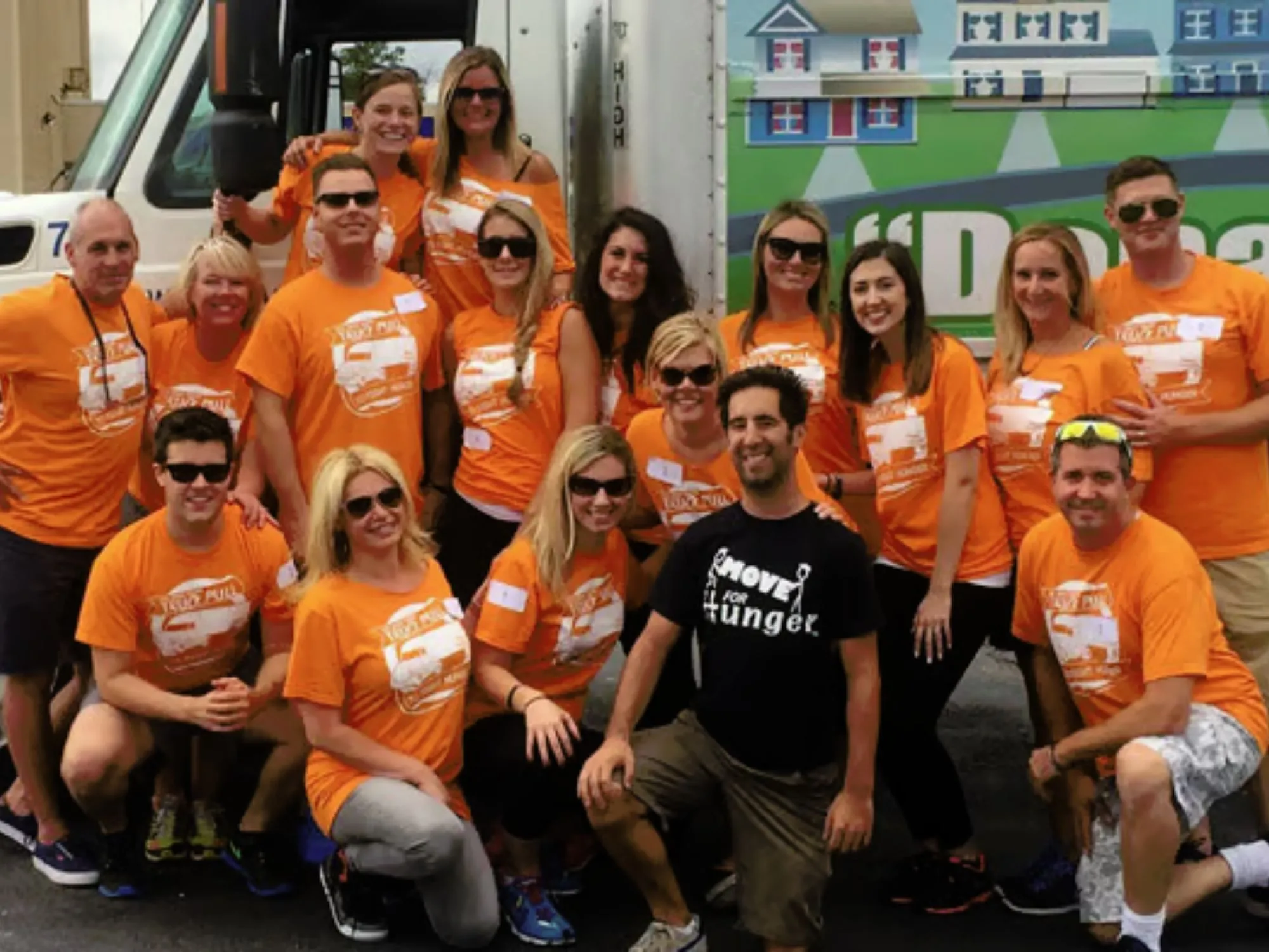 A group smiling wearing matching Move For Hunger orange shirts 