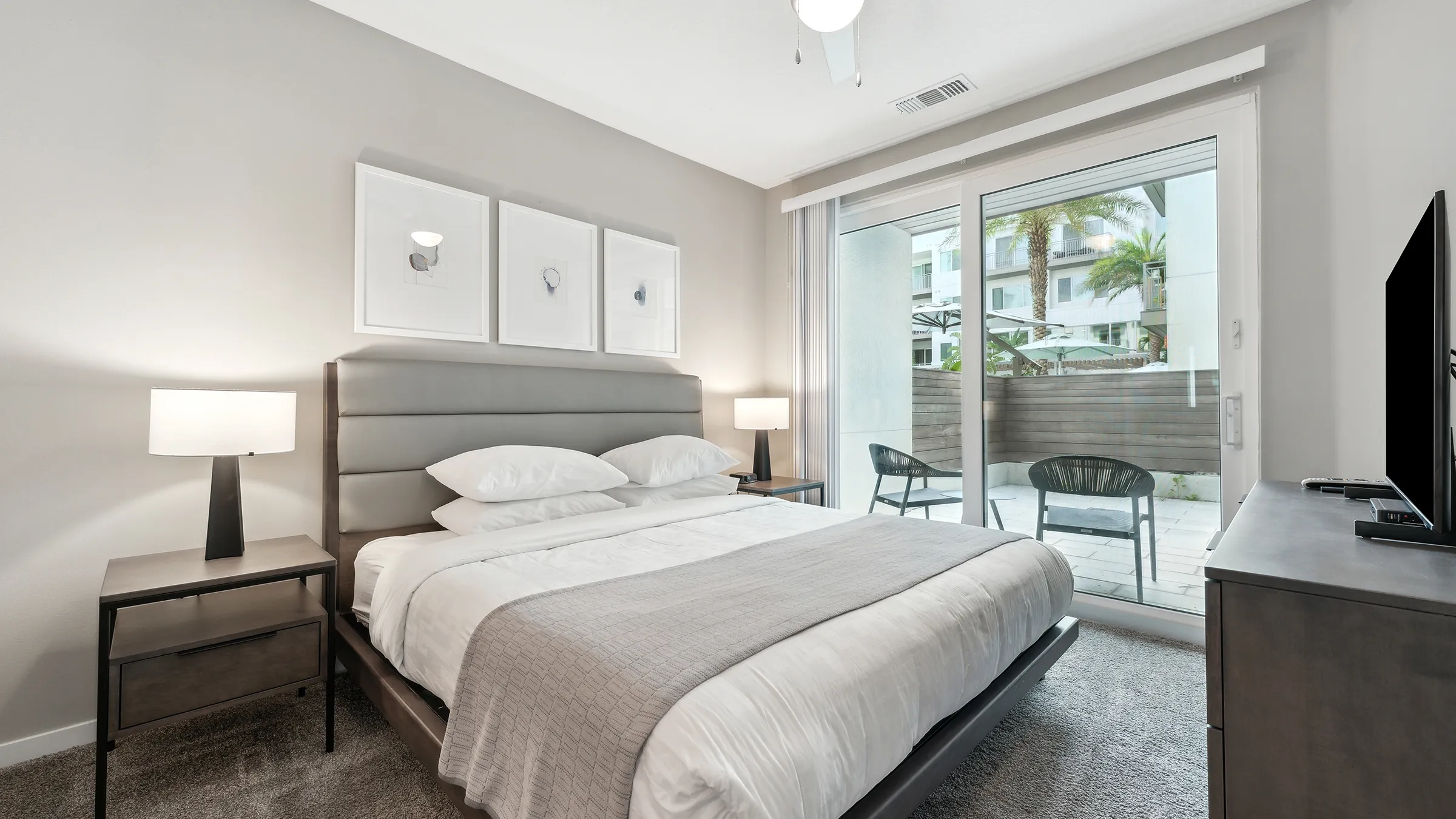 furnished apartment bedroom with upholstered headboard, glass patio door, and TV in Tampa, FL