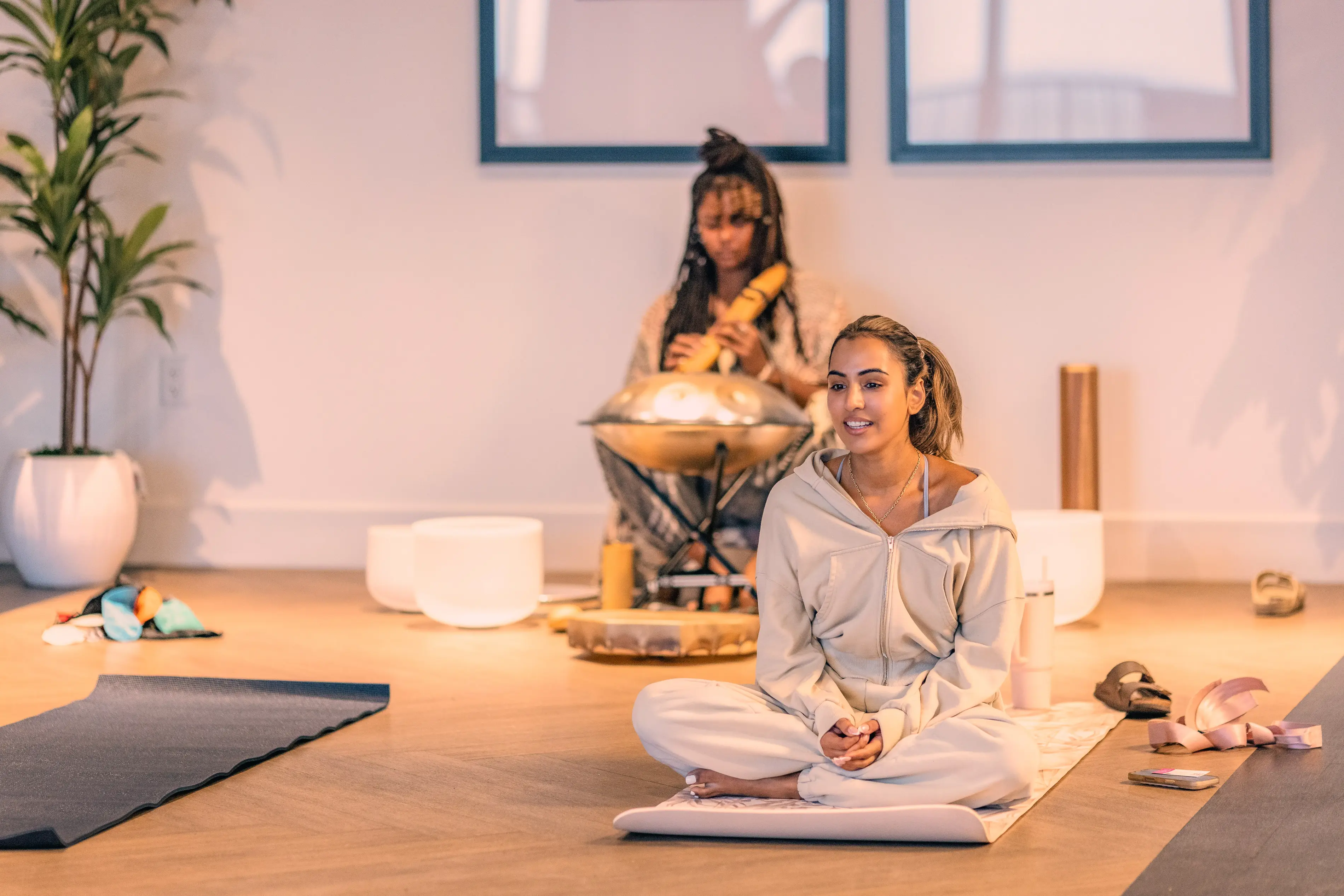 a woman sitting on a mat with a person playing a musical instrument