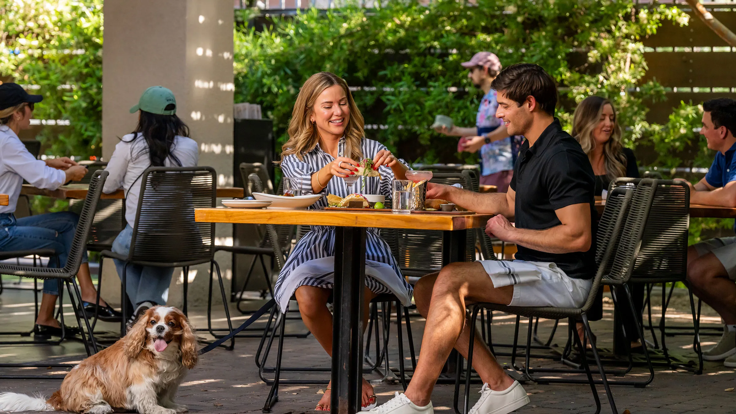 a man and woman sitting at a table with food and a dog