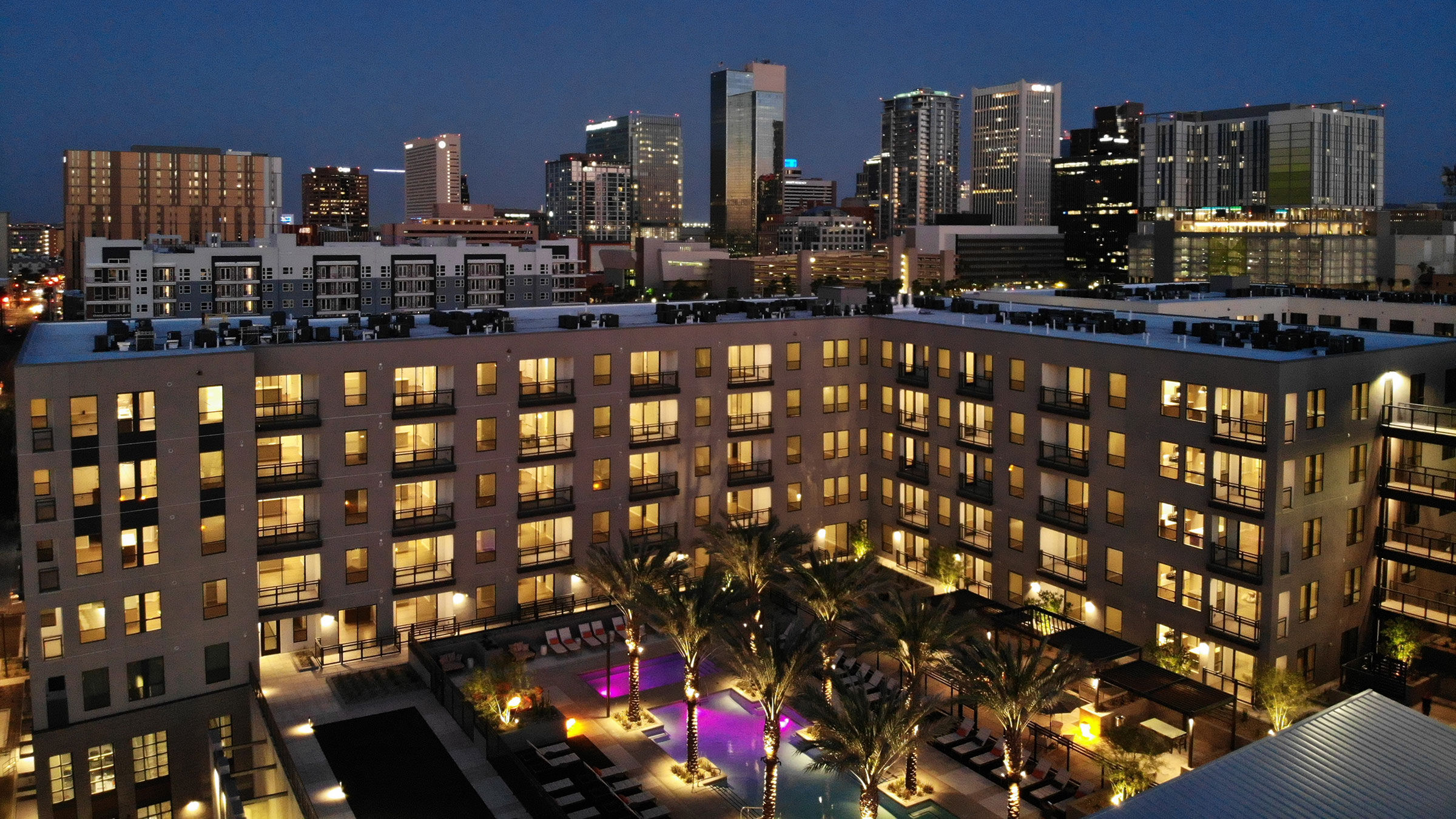 a building with palm trees and a city skyline at night
