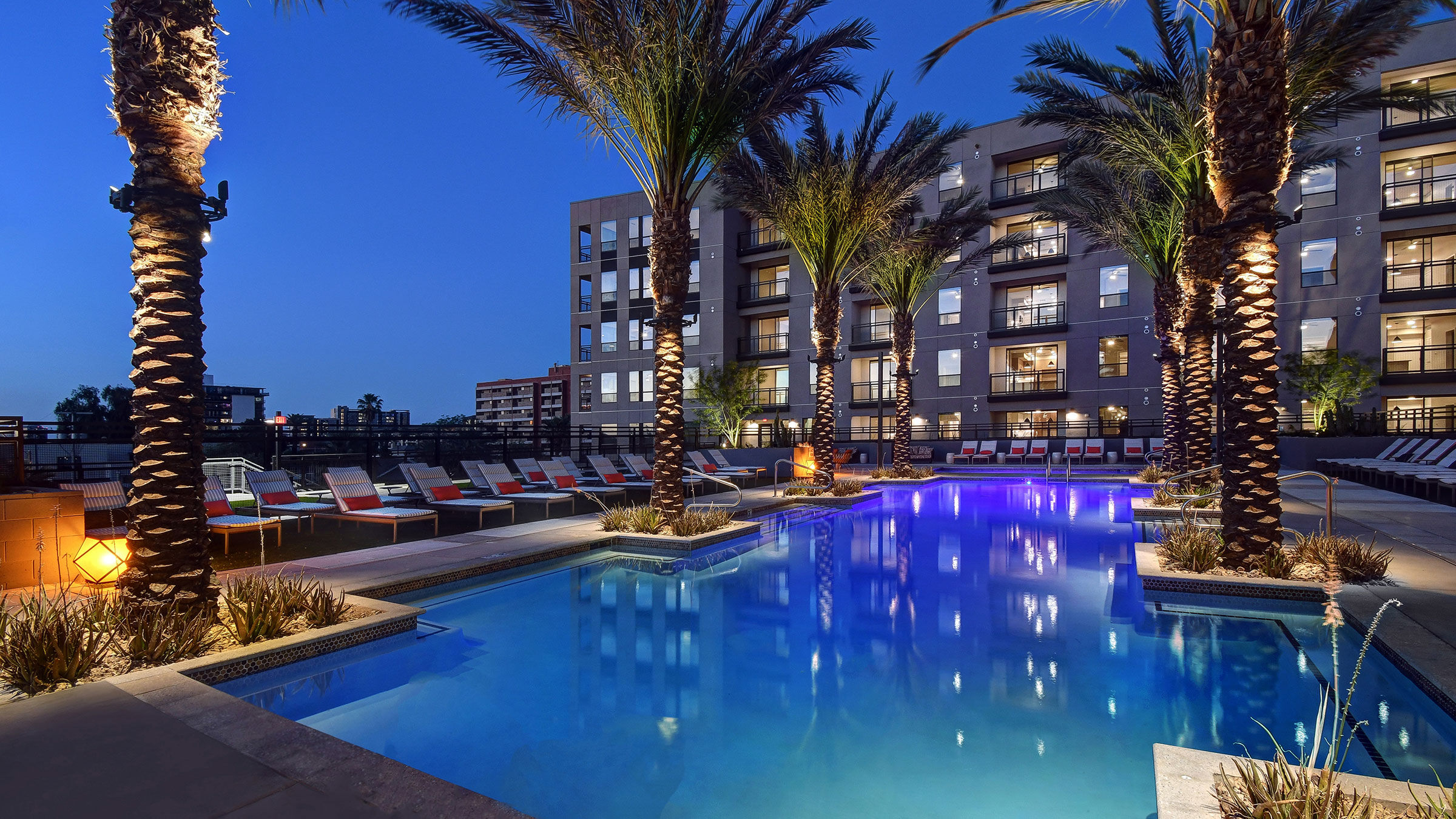 a pool with palm trees and lounge chairs in front of a building