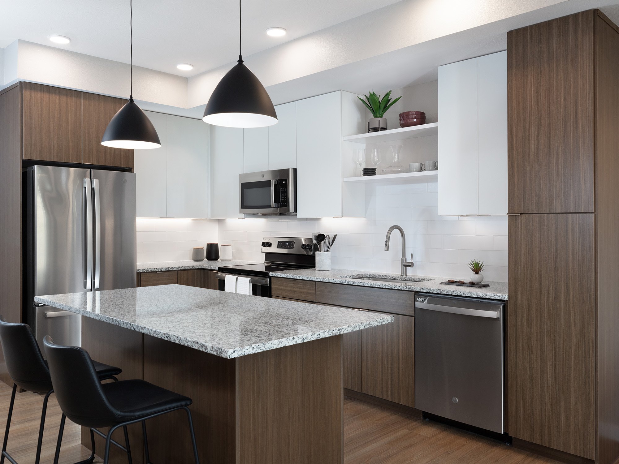 Kitchen with white and light wood cabinets, island with quartz countertop and black leather barstools, stainless steel appliances, and views into living room
