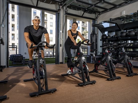 Man in blue shirt using fitness machine with woman in light blue shirt behind him