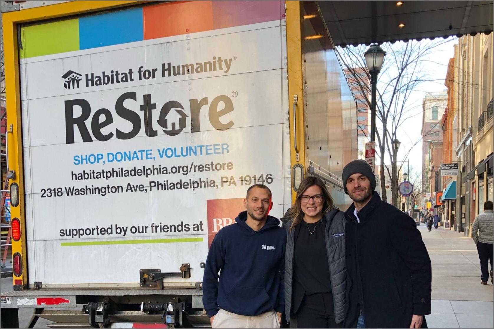 One woman, two men standing in front of moving truck on sidewalk for Habitat for Humanity ReStore 