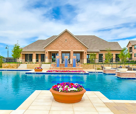 Las Colinas Pool with clubhouse in background, flower pot in foreground with white and pink flowers