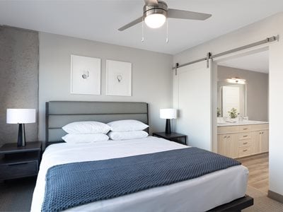bedroom with king-sized bed, gray headboard, blue blankets and views into bathroom area