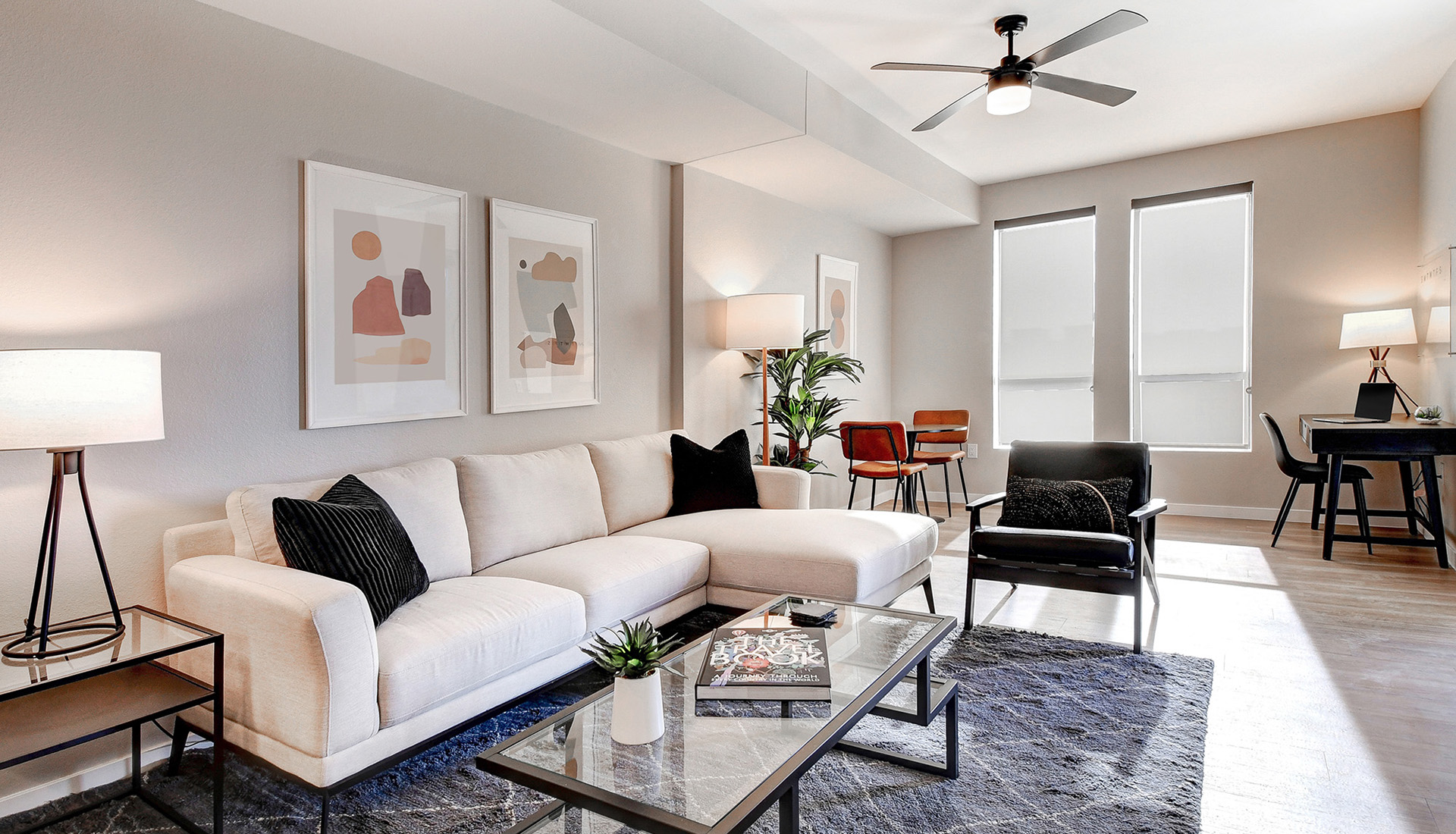 Apartment with cream colored couch, glass coffee table, dining table with two orange chairs, black lounge chair