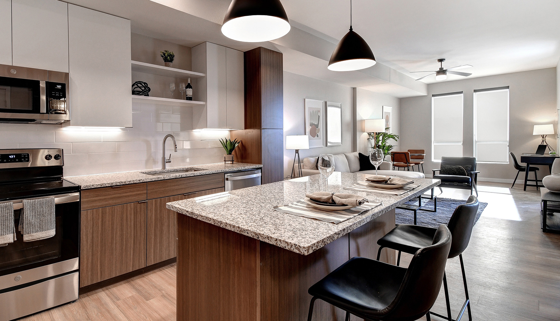 Kitchen with white and light wood cabinets, island with quartz countertop and black leather barstools, stainless steel appliances, and views into living room