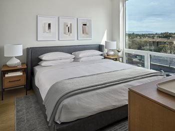 Bedroom with king-sized bed, gray headboard, white linens and pillows, gray throw blanket and oak dresser with tv