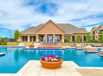 Resort-style pool with clubhouse in background, pink and white flowers in pot in foreground