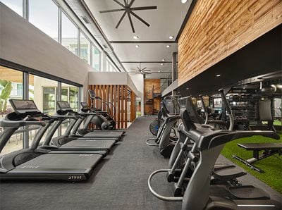 Fitness center with cardio equipment, green turf area with weights, and views to spiral staircase leading up to second fitness level