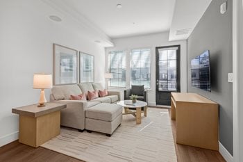 Living Room with gray sofa, white club chair and circular dining table, large windows leading to balcony, tv on oak stand