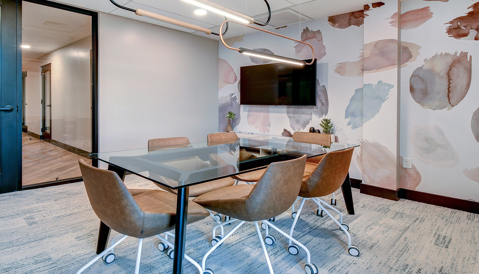 Conference room with glass table, brown leather office chairs, and tv