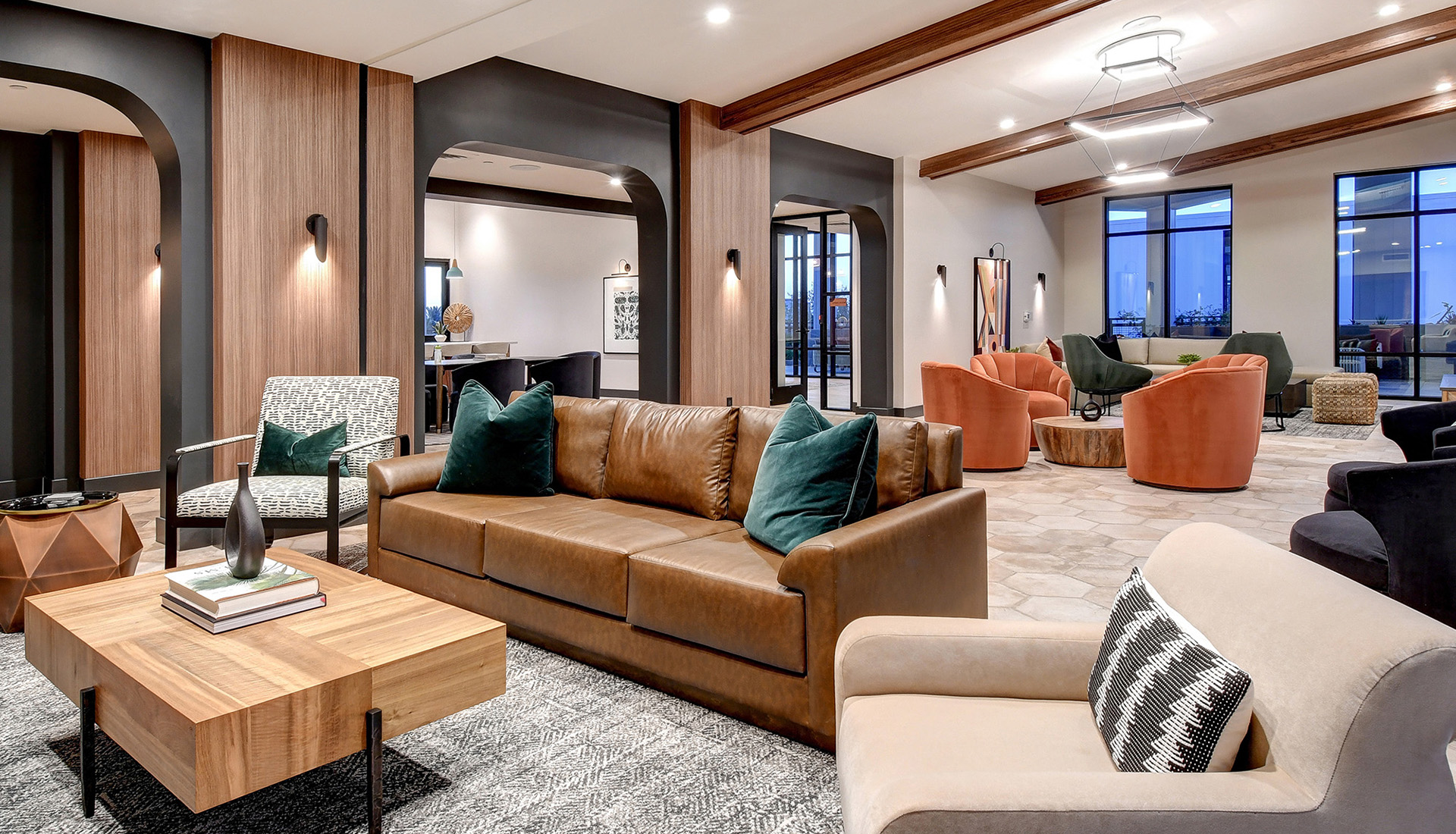 Lounge area with brown leather couch, cream colored chair, wood coffee table, with views into other amenity spaces